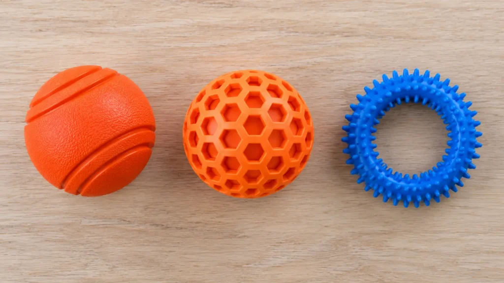 Three rubber dog toy shapes compared for durability — a solid ball, a honeycomb-textured ball, and a spiked ring